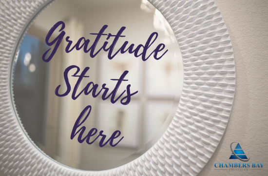 White wall mirror that says "Gratitude starts here" in blue letters.
